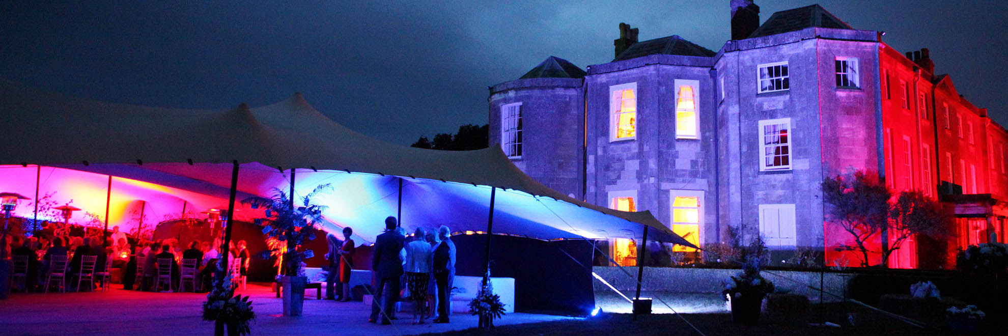 beige stretch tent in from of grand house lit up in red and blue