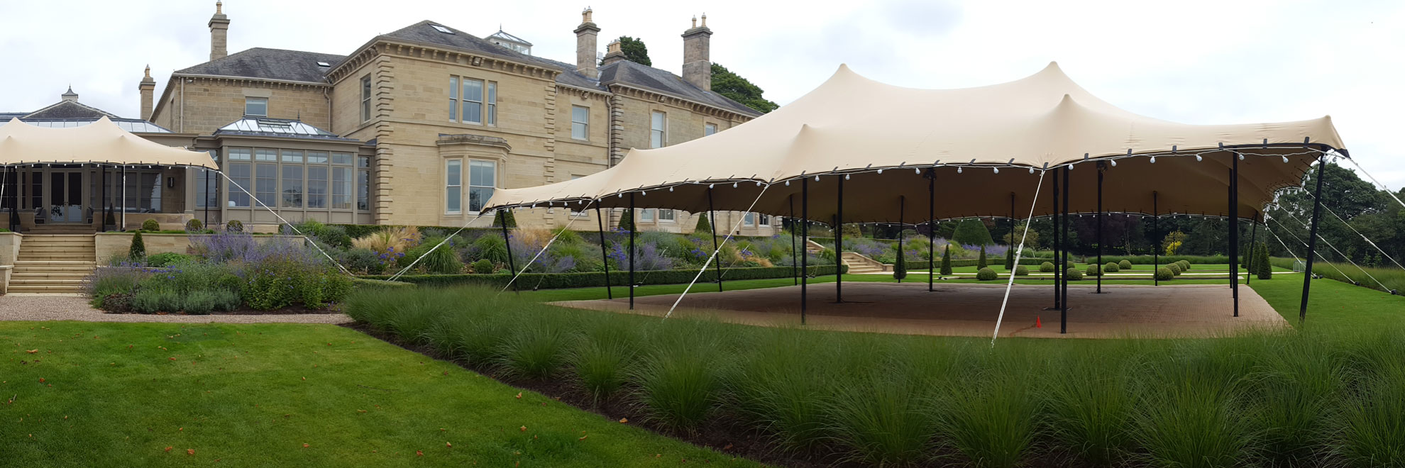 Beige stretch tent on lawn, with matting flooring.