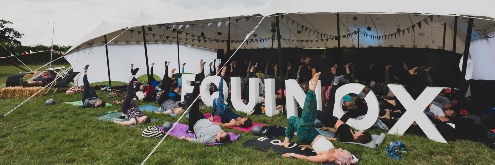 White stretch tent Equinox sign in foreground Yoga lesson in progress