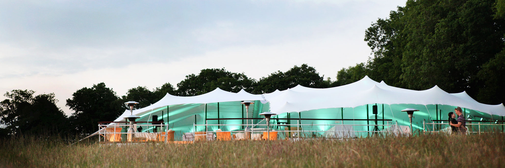 White stretch tent, turqoise lighting inside, dusk, meadow field.