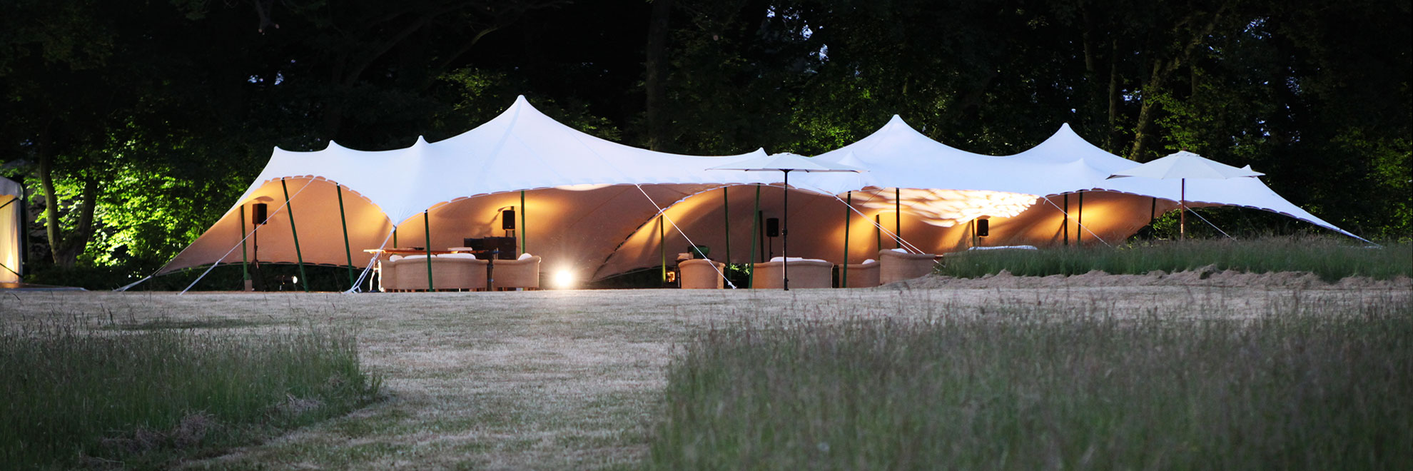 Beige stretch tent in a meadow field lit up at dusk.