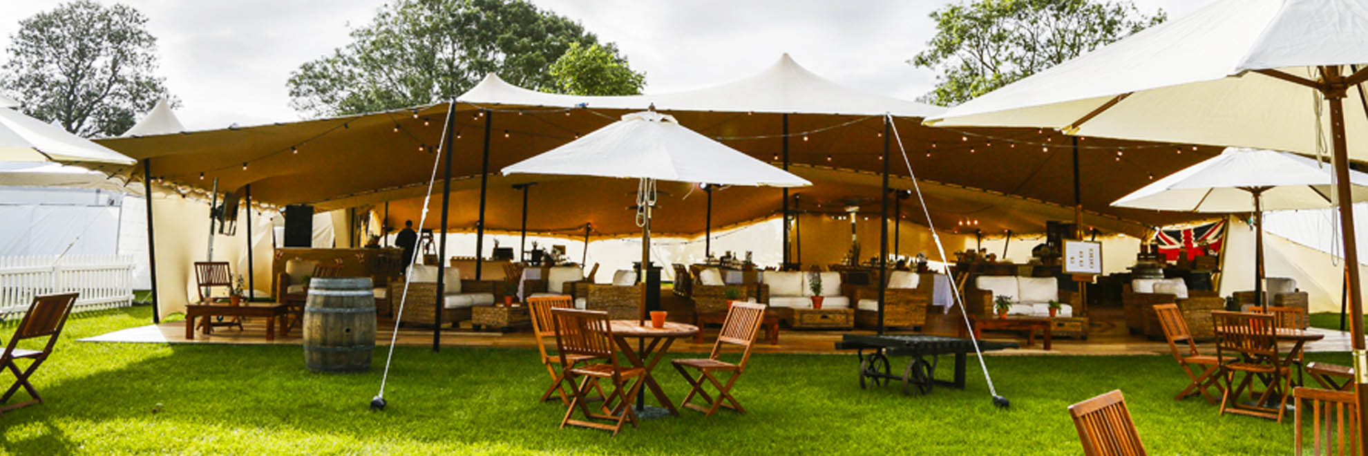 Full_Furnishings_Stretch_Tent_10x15 Beige Stretch Tent, Green lawn, Small tables, umbrellas