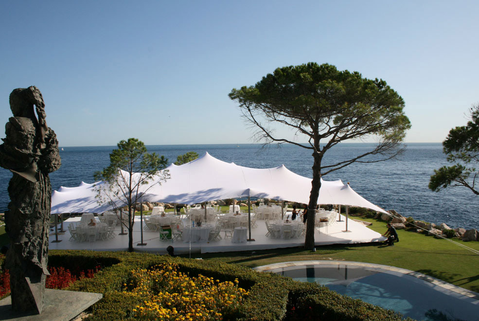 White Stretch Tent in a field with people in it, white sofas and blue sofas.