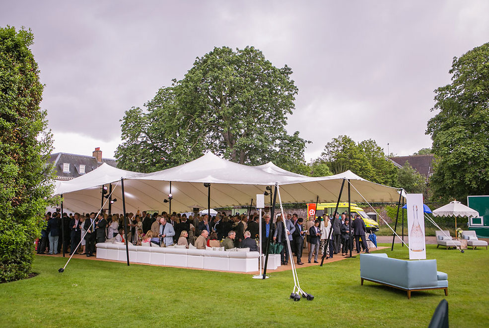 White Stretch Tent in a field with people in it, white sofas and blue sofas.